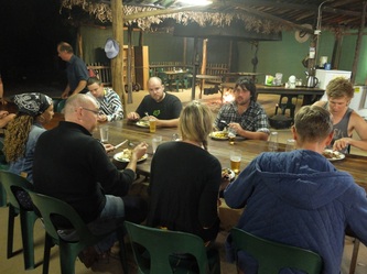 Dining area photo - guests are sitting at a timber table and the campfire is in the background 