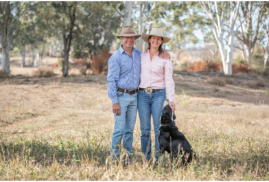 Picture of Carl Hendrick and partner Lyn Eather with Jose the border collie standing in paddock with buffel grass and brigalow and tozet box trees.
